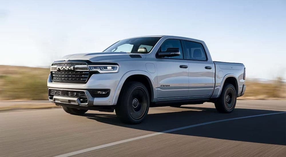 A white 2025 Ram 1500 Ramcharger driving down a road from a dealer with a Ram 1500 for sale.