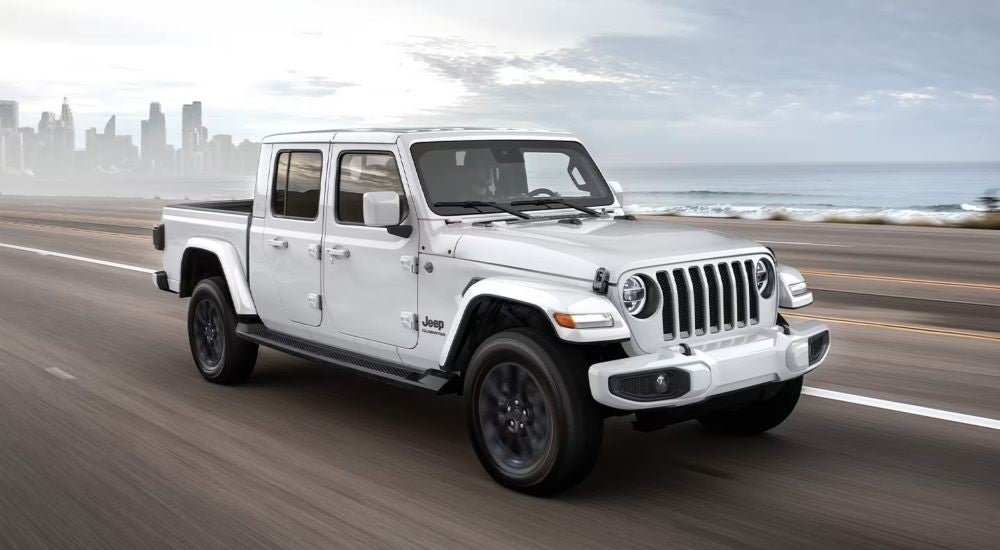 A white 2020 Jeep Gladiator driving from a dealer with used trucks for sale.
