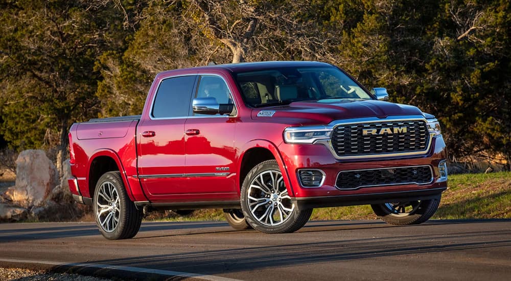 A red 2025 Ram 1500 Tradesman driving down a road from a dealer with a Ram 1500 for sale.