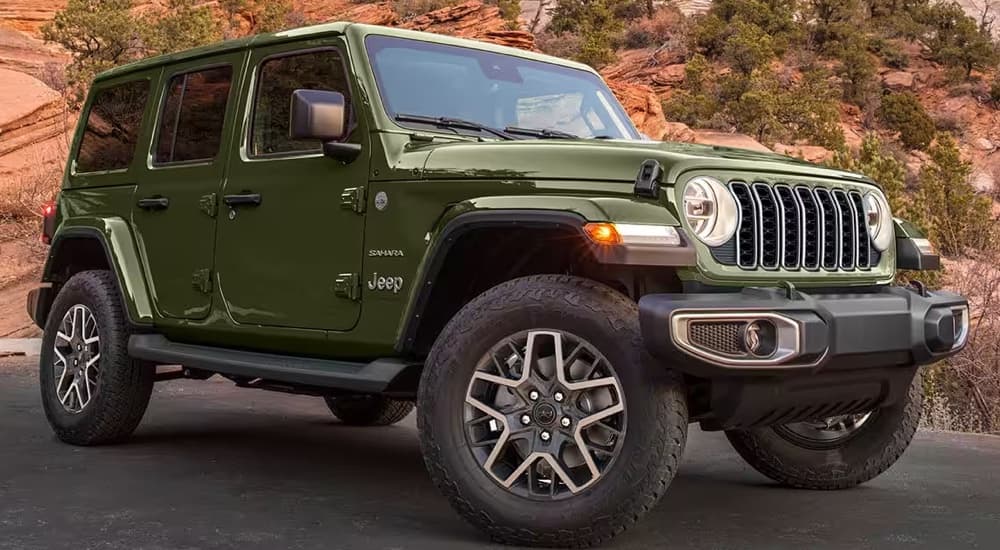 A forest green 2024 Jeep Wrangler Sahara parked outside near a Jeep dealer.