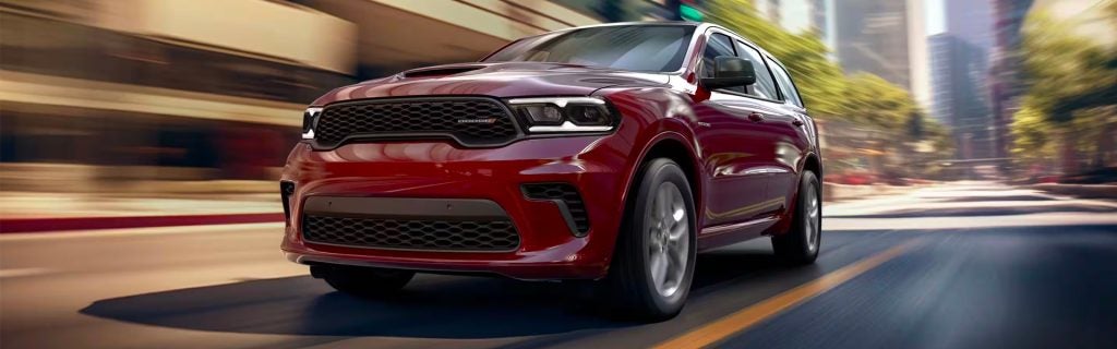 A red Dodge Durango speeding through a city street with a blurred background.