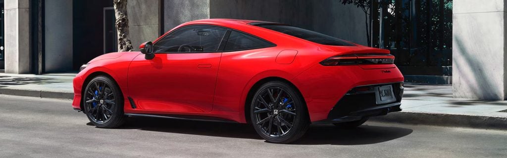 Red Honda sports coupe parked on a city street in front of a modern building.