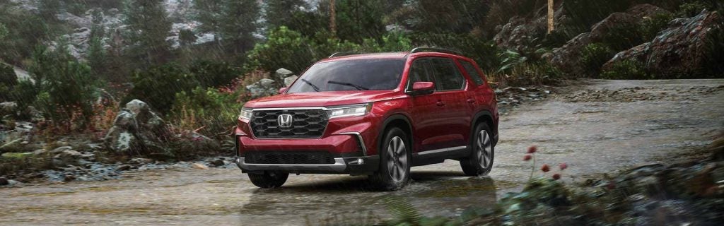 Red 2026 Honda Pilot driving through a rainy forest trail.