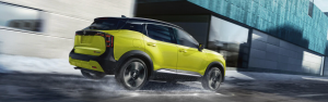 Lime green SUV driving quickly on a snowy city street beside modern buildings.