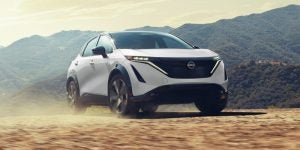 2025 Nissan ARIYA driving on a scenic mountain road near Indianapolis, showcasing its sleek electric SUV design and modern LED headlights.