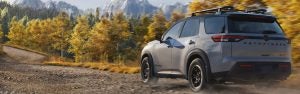 Gray Nissan Pathfinder driving on a gravel forest trail with autumn trees.