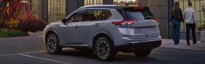A Nissan Rogue parked in front of a building with two people walking away from it.
