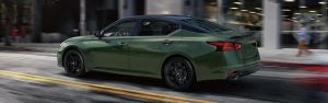 Green Nissan sedan driving on a city street with blurred motion.