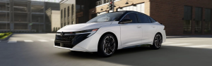 White 2026 Nissan sedan driving through a city street near brick buildings.