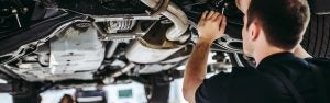 Mechanic inspecting a car’s undercarriage in a repair shop.