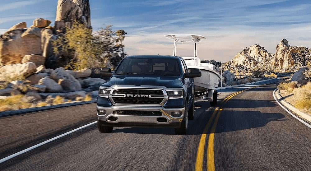 A blue 2023 Ram 1500 towing a boat on an open road.