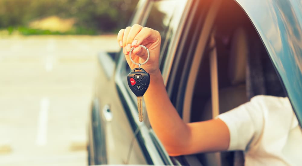 A person holding a car key out of the window of a car at a Certified pre-owned Chrysler dealer.