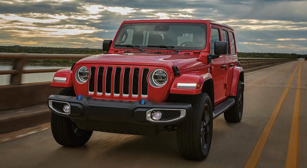 A red 2023 Jeep Wrangler for sale near you is shown from the front driving on an open road.