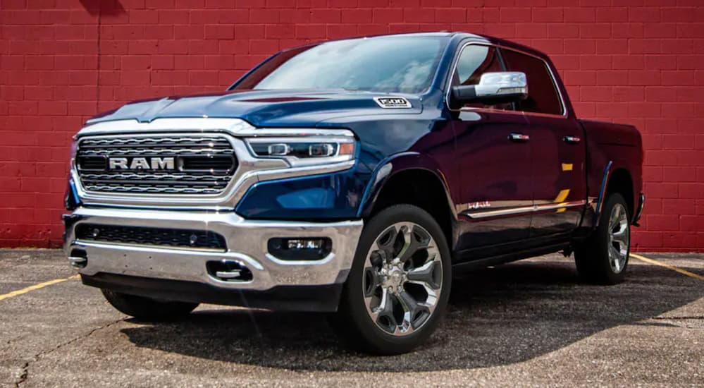 A blue 2021 Ram 1500 parked in front of a red brick wall near a Ram dealer.