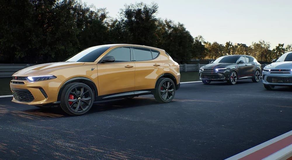 Side view of a yellow 2023 Dodge Hornet driving away from an SUV dealer nearby