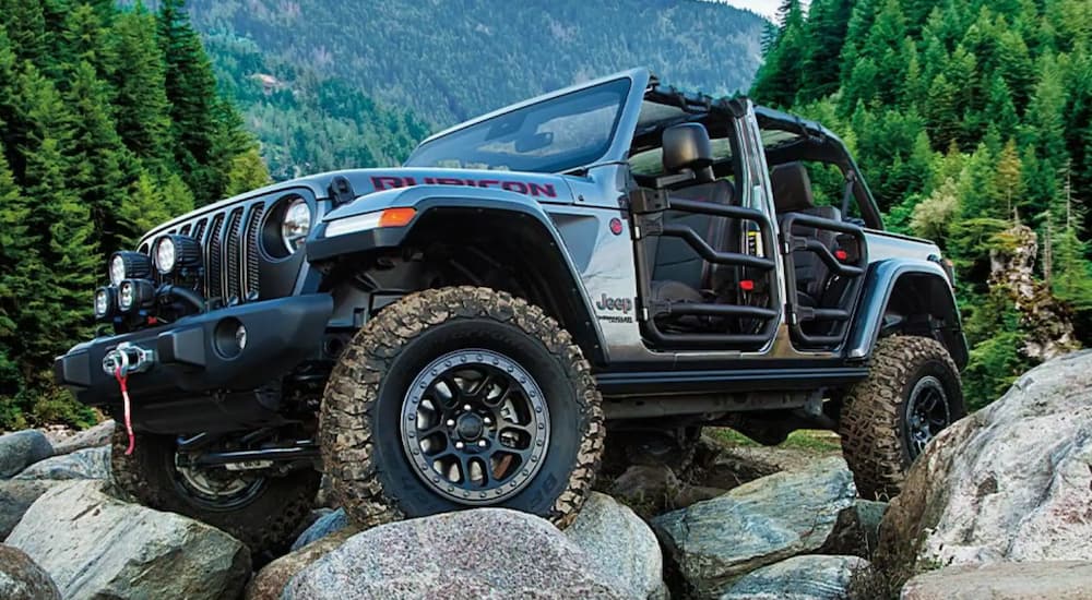 A grey 2021 Jeep Wrangler Rubicon off-roading over large rocks in a stream bed.