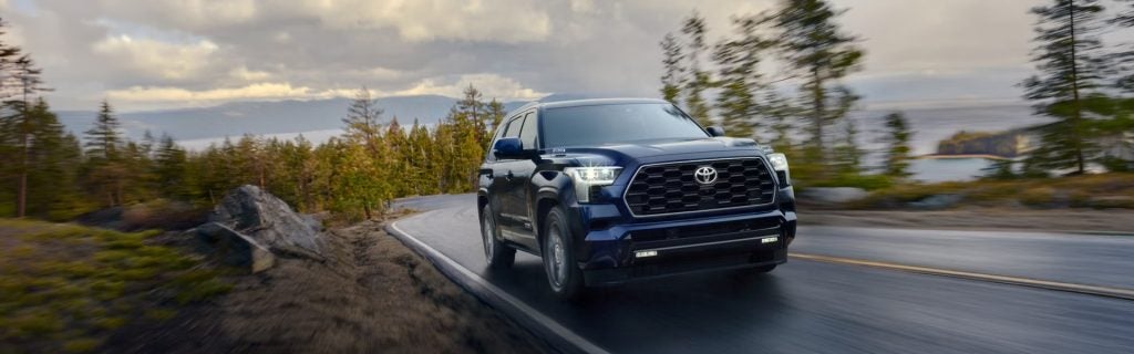 Dark blue Toyota Sequoia driving on a winding mountain road surrounded by trees.