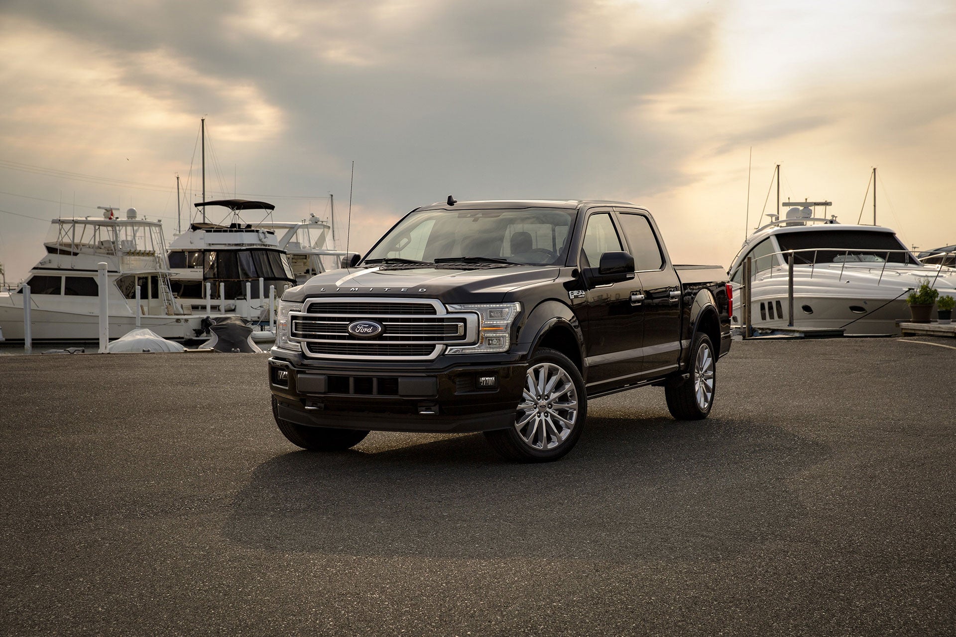 Ford F-150 parked at pier with boats and a sunset in the background