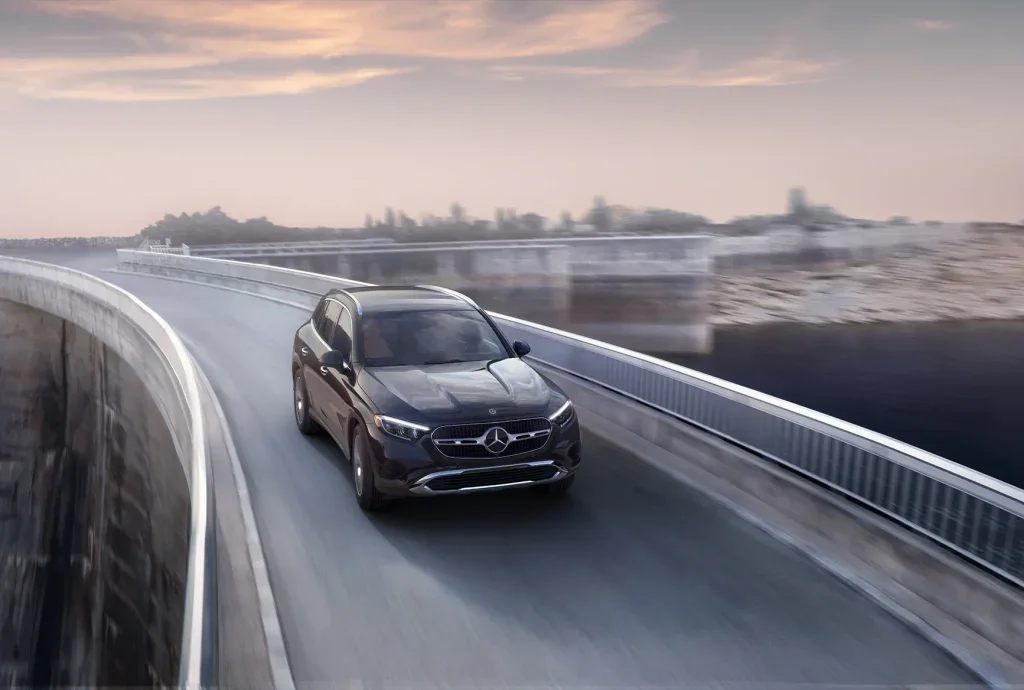 Dark 2026 Mercedes-Benz GLC driving on a curved elevated road, capturing the SUV’s smooth performance and refined driving experience.