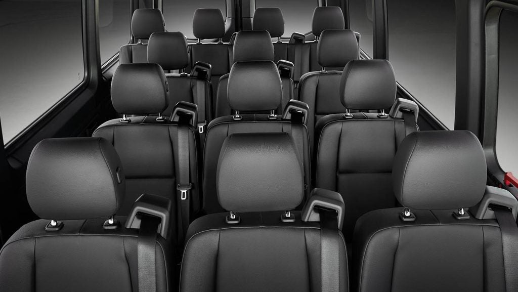 Interior view of a Mercedes-Benz Sprinter Van showing multiple rows of black passenger seats.