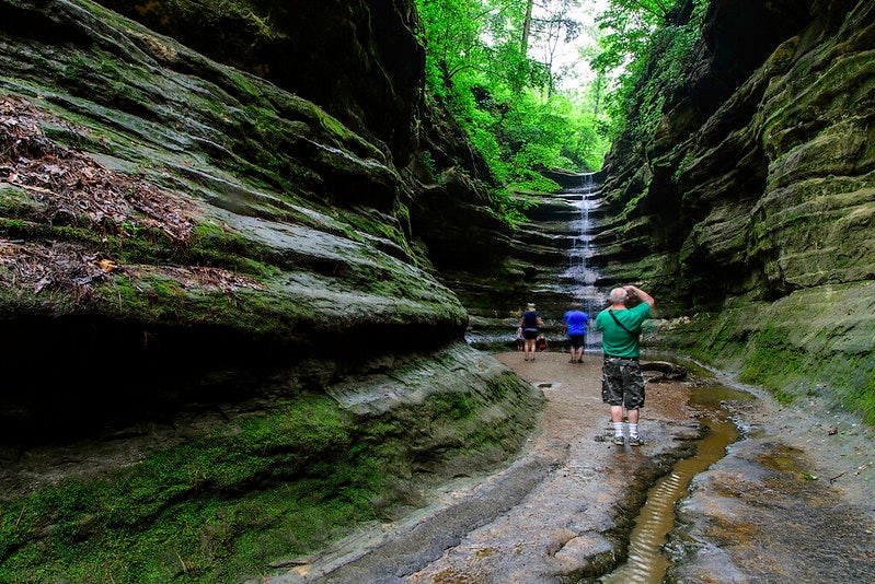 Visitors hiking through a canyon toward a waterfall at Starved Rock State Park.