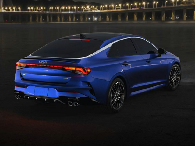 A blue Kia K5 parked near the water at night time