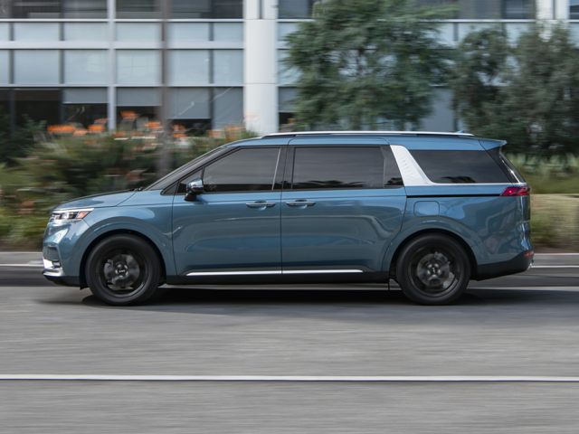 A blue Kia Carnival driving a car outside of a building
