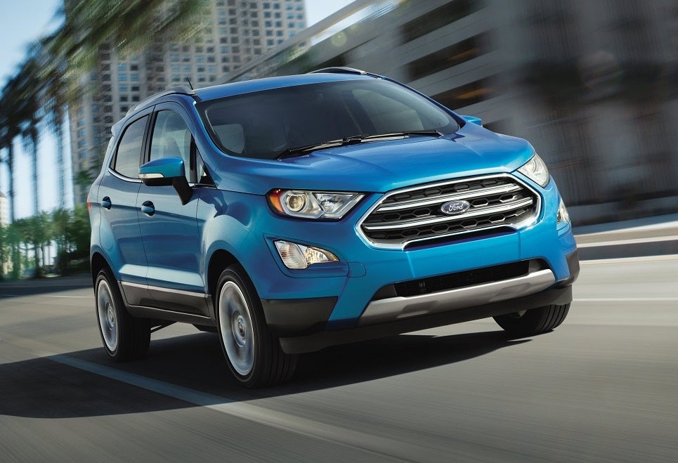 Blue Ford EcoSport driving in the city past buildings and palm trees