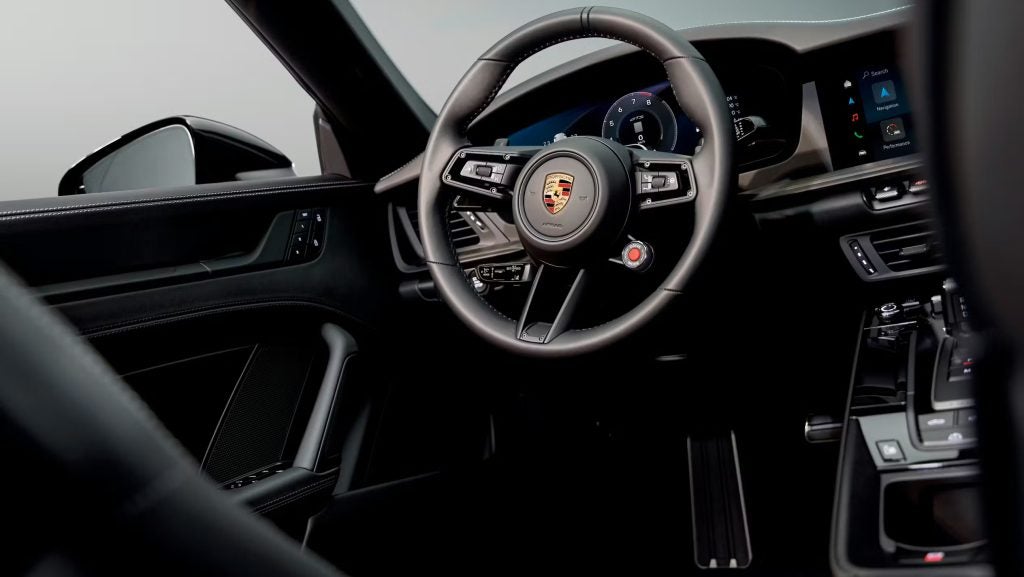 Porsche 911 interior view with steering wheel and digital displays, illustrating longevity and why the Porsche 911 defines the modern sports car.