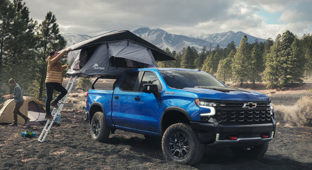 A blue Chevy Silverado is parked as a couple sets up a campsite around it.
