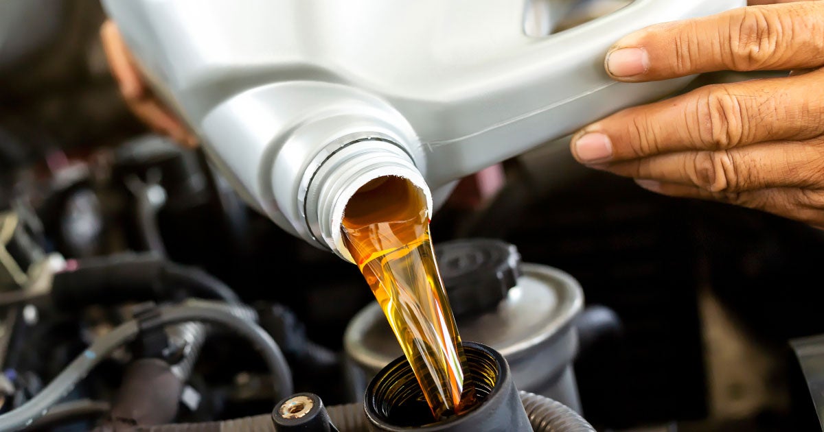 Close-up of a service technician refilling oil in a vehicle's engine.
