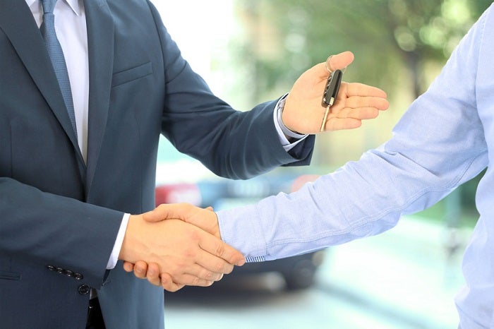 Car salesman handing over the keys for a new car to a young busi