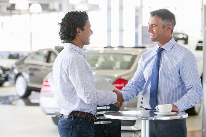 Salesman and customer shaking hands at table in car dealership showroom