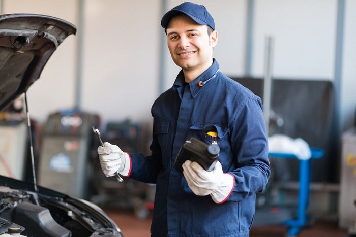 Auto mechanic putting oil in a car engine