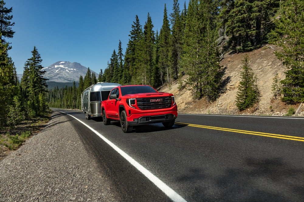 GMC Sierra 1500 Elevation Crew Cab Short Box in Cardinal Red with 20-inch Six-Spoke High Gloss Black Painted Aluminum Wheels; Hauling/Towing Airstream Trailer/Camper; 3/4 Passengers side Front; Road shot/motion; Forest and Mountains in background