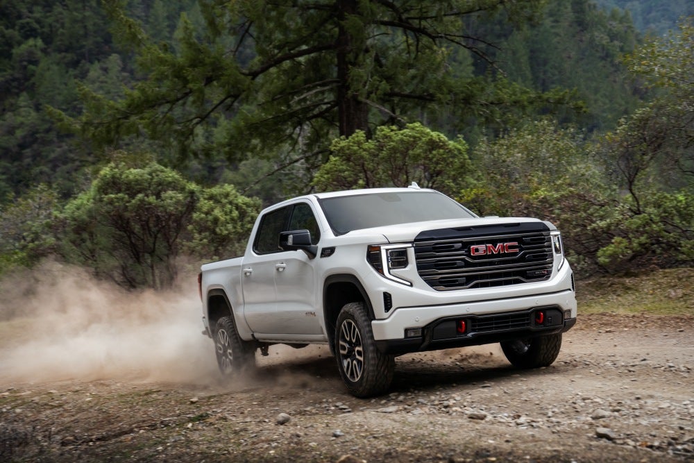 White GMC Sierra 1500 driving on dirt road in forest