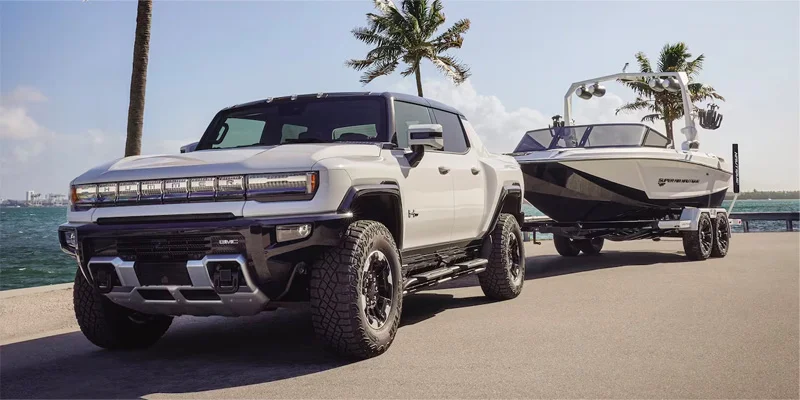 Hummer EV Pickup in white pulling boat trailer at a boat launch
