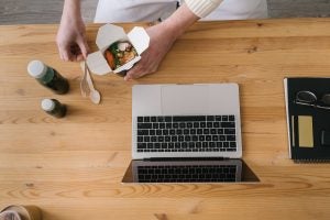 Bird's-eye-view image of a person opening up Chinese food take-out box by his laptop.
