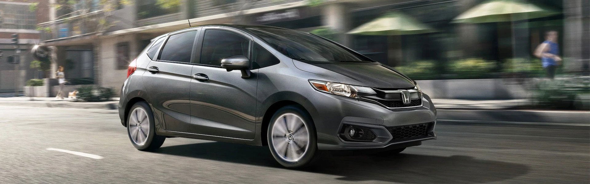 Gray Honda Fit hatchback driving on city street, sleek design, modern urban background | Priority Honda Roanoke