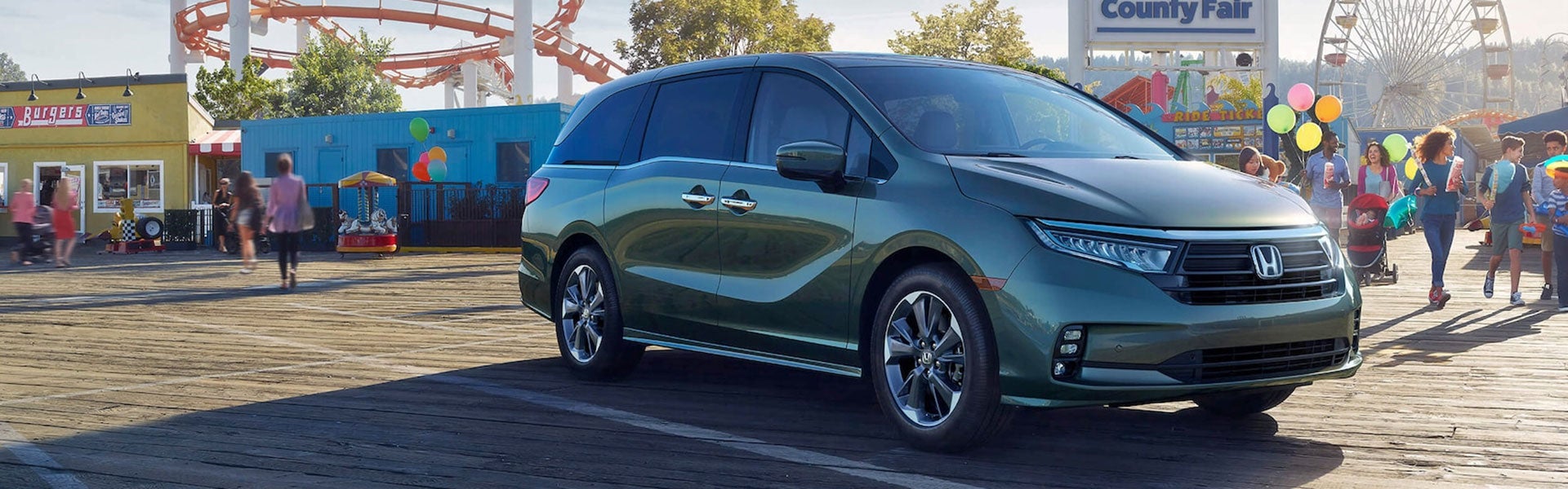 Green Honda Odyssey minivan parked at county fair with Ferris wheel and colorful balloons in background
