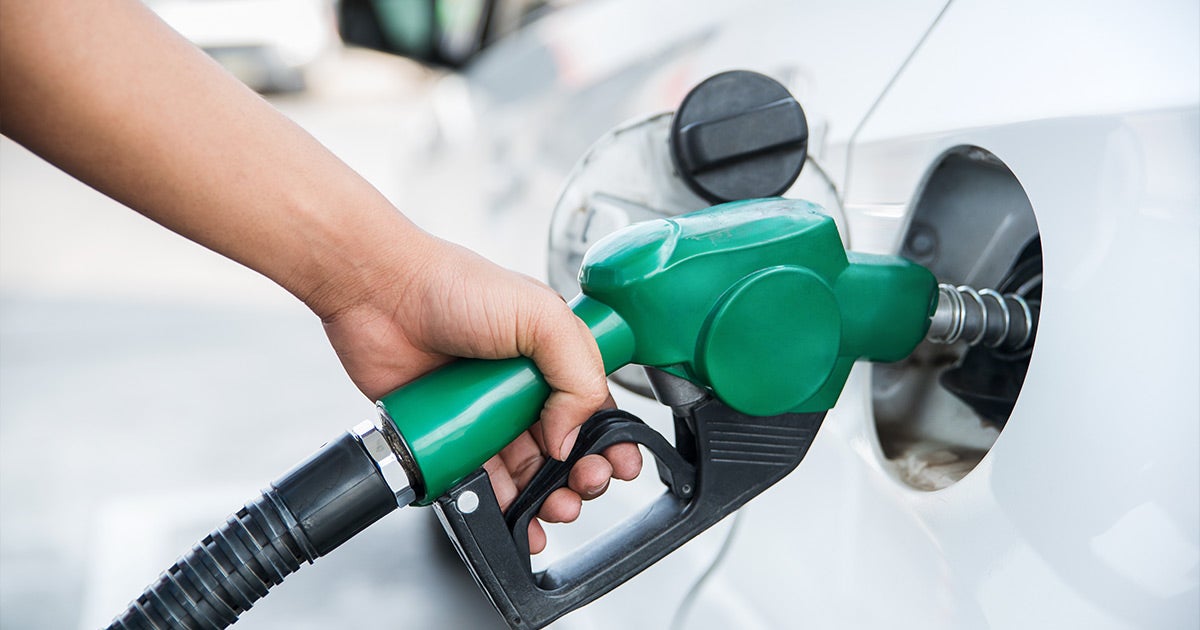 Green fuel nozzle pumping gas into white vehicle at filling station, close-up of refueling process