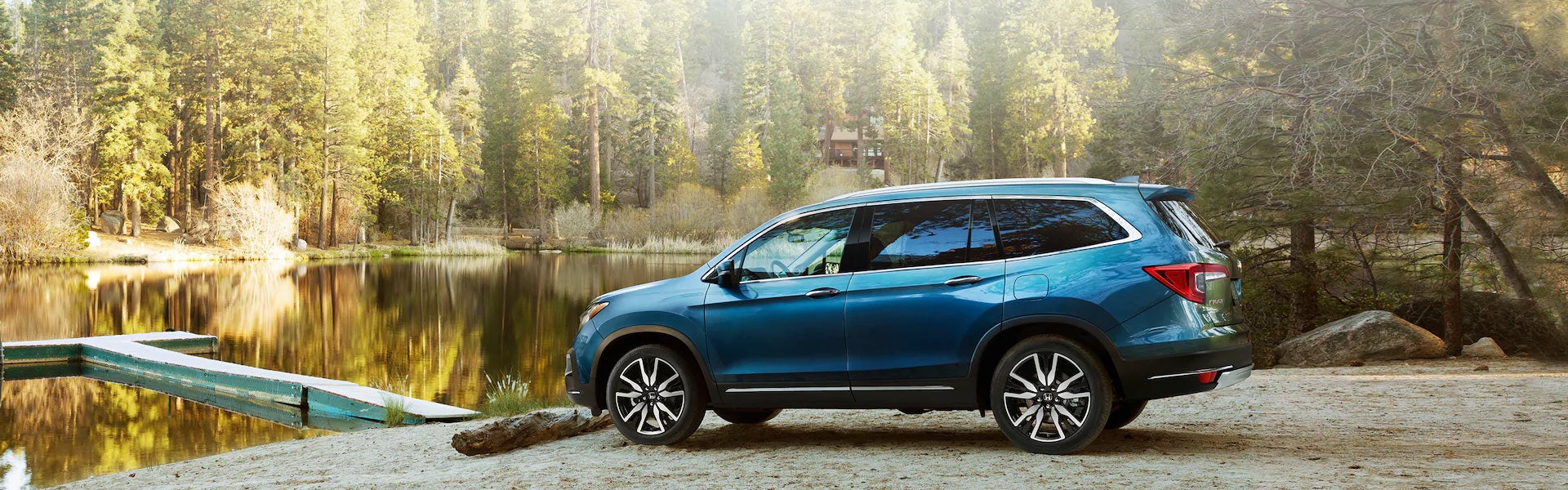 Blue Honda Pilot SUV parked by scenic forest lake with boat launch, showcasing rugged outdoor capability - Priority Honda Roanoke