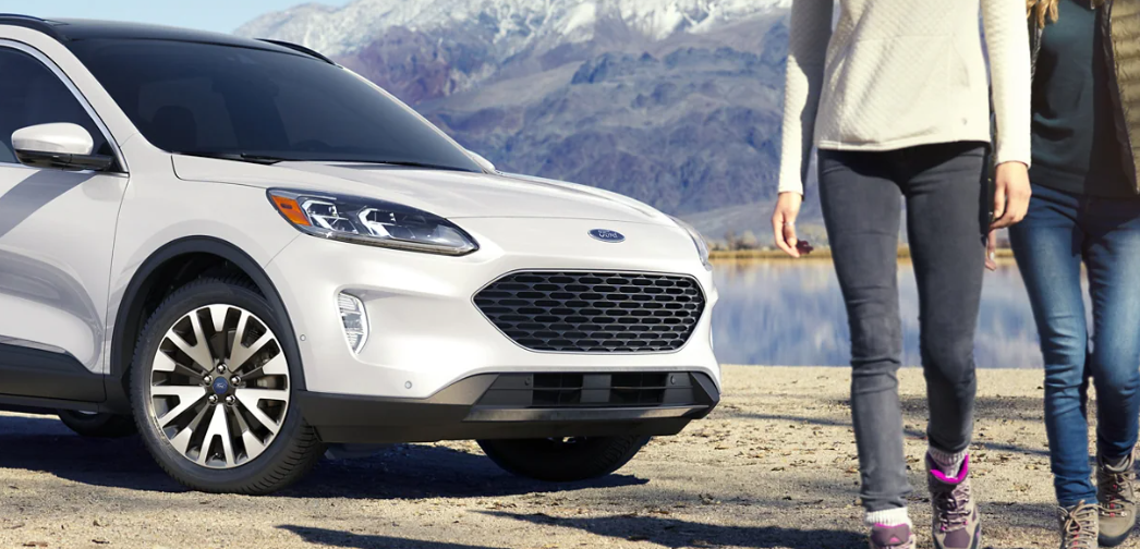 Two women standing next to a Ford Escape in the mountains