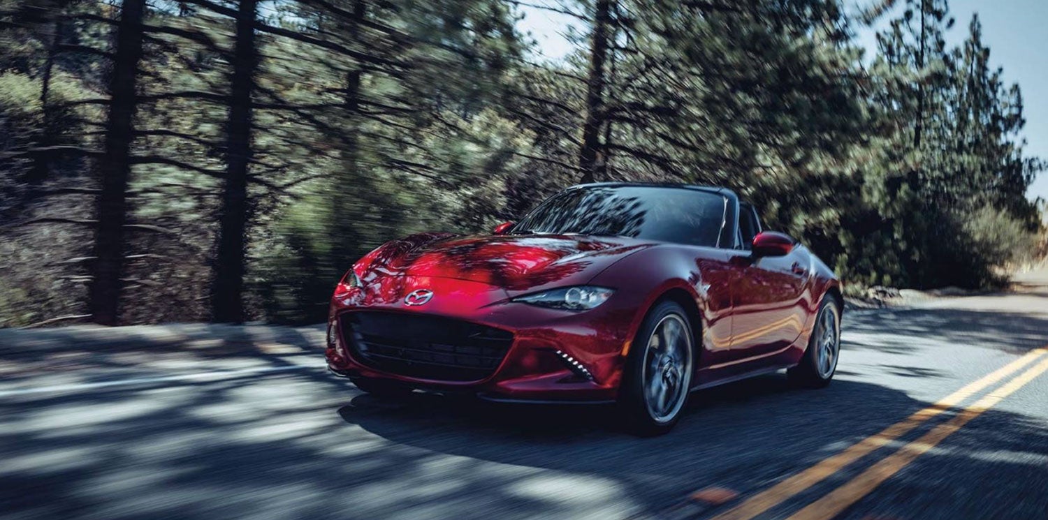 Red Mazda MX-5 Miata Club on a tree-lined road with the top down