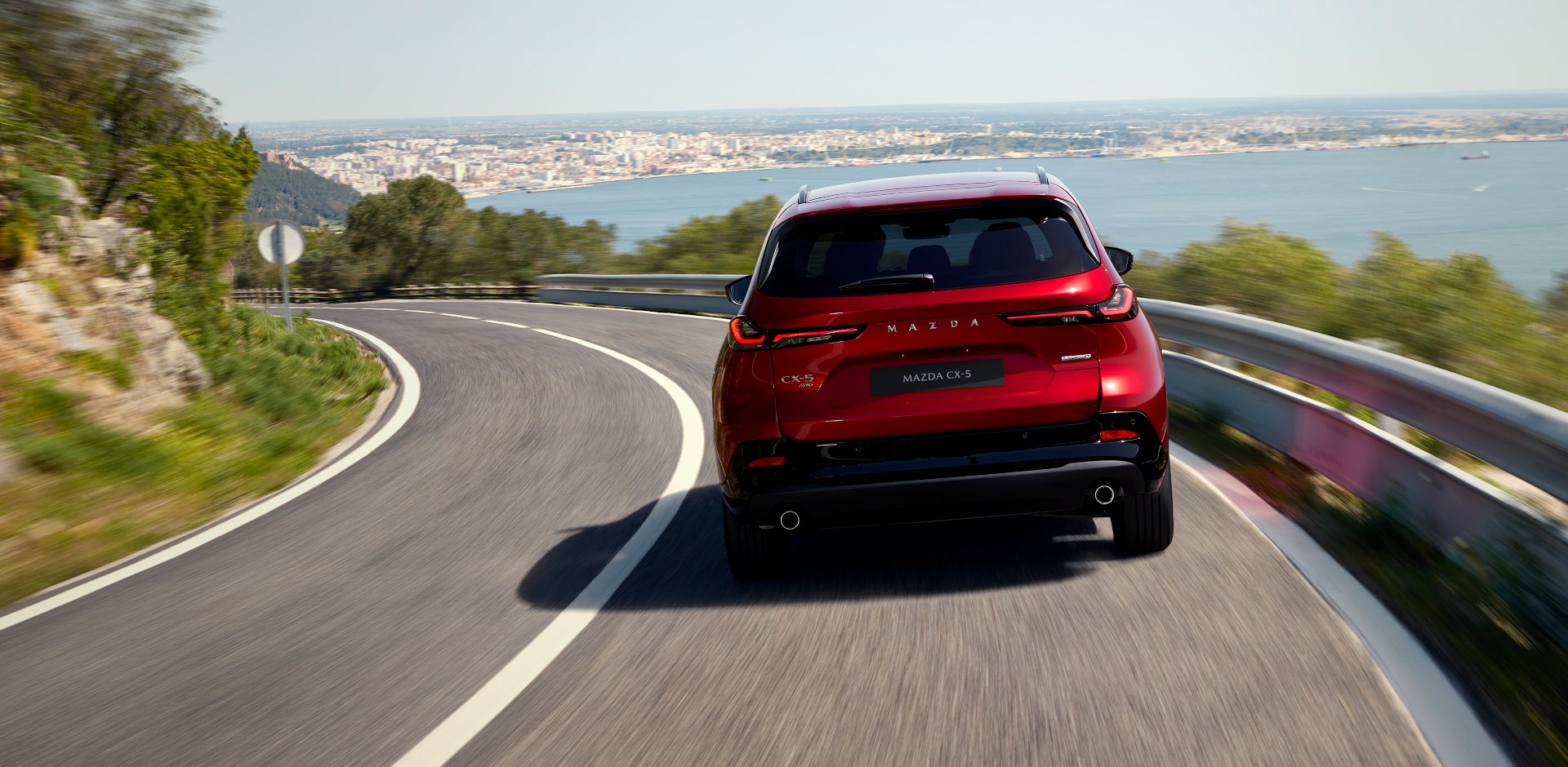 Rear three-quarter view of the 2026 Mazda CX-5 in red on a winding road