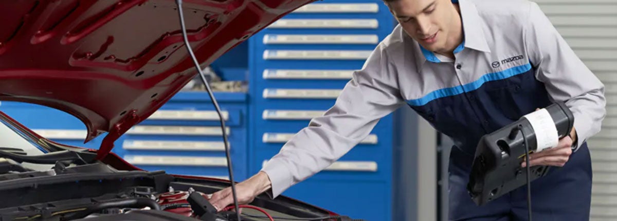 A mechanic inspecting a Mazda car for potential car leaking issues in the engine bay.