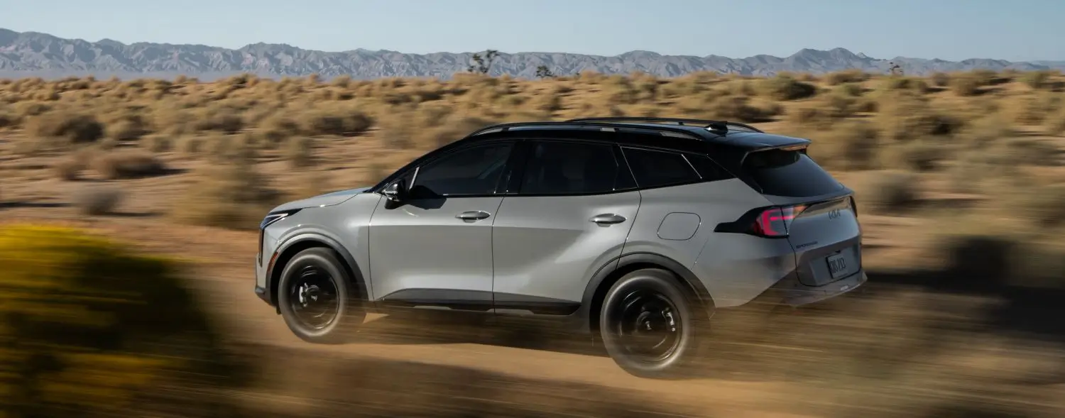 Un elegante SUV Sportage plateado recorre a toda velocidad un paisaje desértico, con montañas al fondo, mostrando su diseño moderno y su movimiento dinámico.