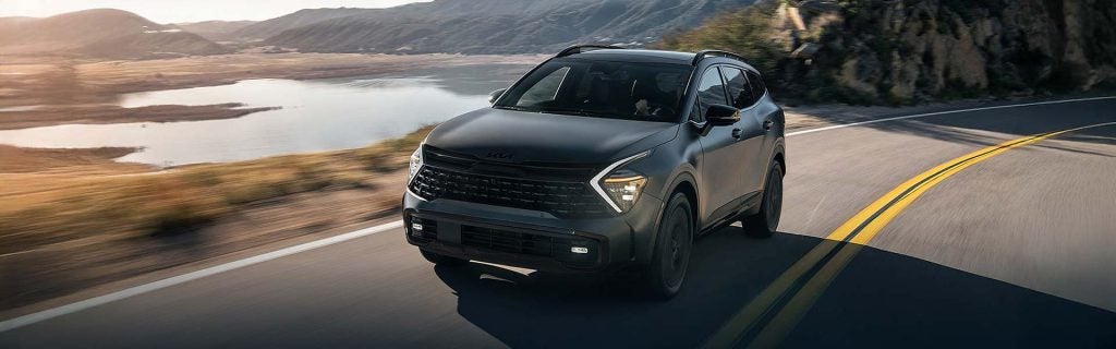 Kia Sportage Hybrid SUV driving along a scenic road by a lake.