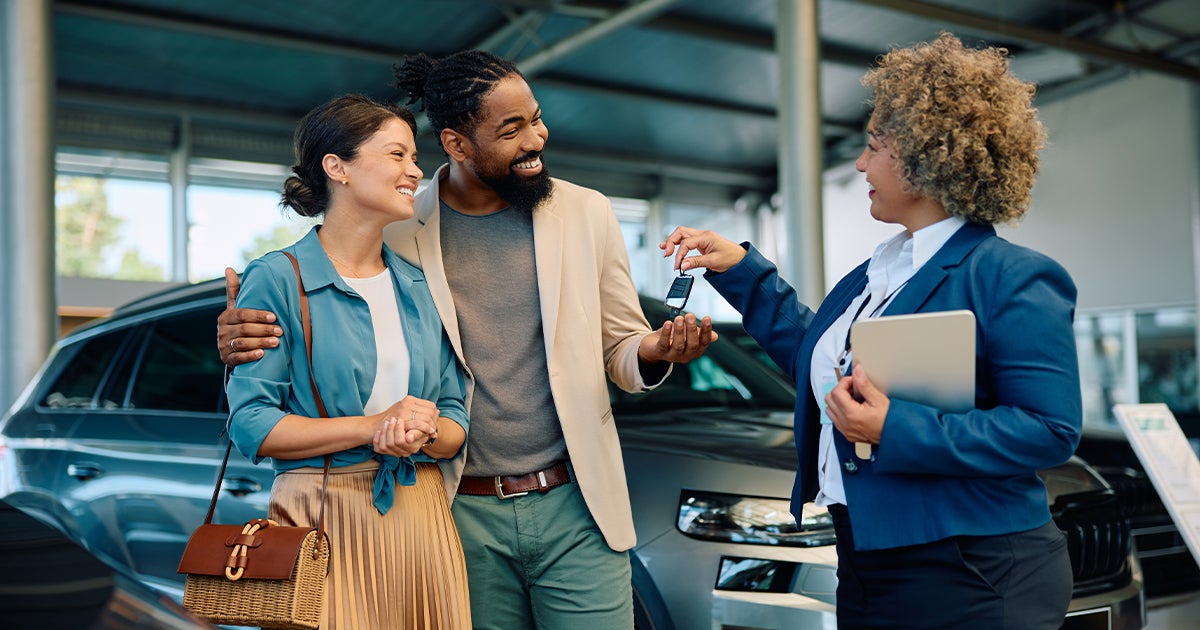 A car salesperson handing a happy couple keys to their new vehicle.