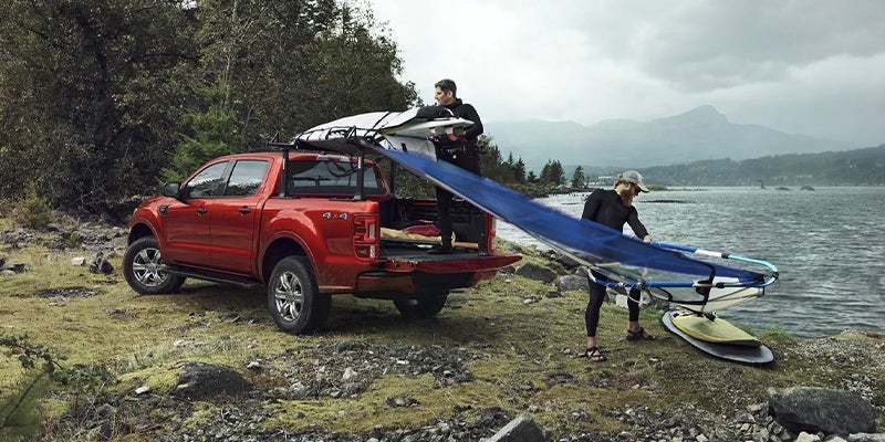 two surfers off-loading their brand new red 2023 Ford Ranger with their surfboards getting ready to hit the waves